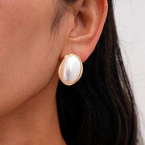 Gros plan détaillé d'une boucle d'oreille en perle ovale dorée portée par un mannequin