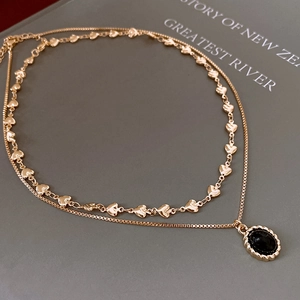 Detail of double-layer gold necklace featuring heart links and a black oval stone pendant