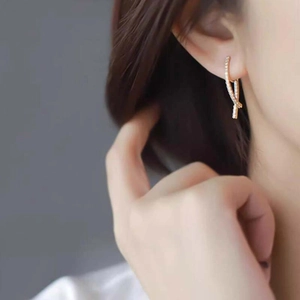 Close-up of golden crossover knot earrings with micro-pave zircons on model ear