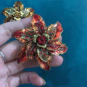 Vintage red enamel flower brooch with gold petals and rhinestones on green background