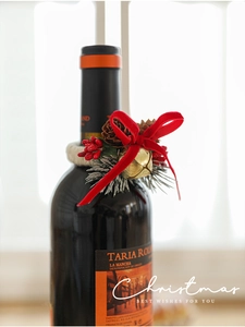 Close-up of Christmas wine bottle ring with red bow, pine cones and golden bells decoration