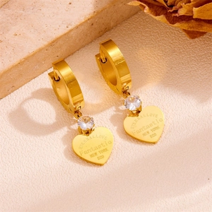 Detail of gold heart earrings with zircon inlay and engraved text on textured surface