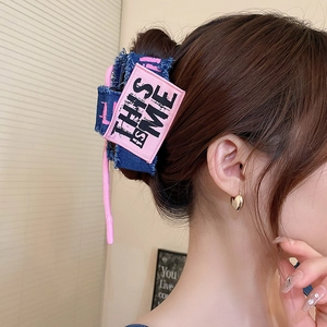 Detail of denim bow hair claw clip with pink 'THIS IS ME' patch and frayed edges