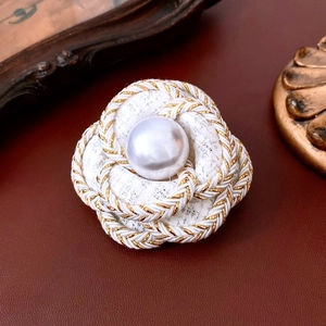 Close-up of white tweed camellia brooch with gold thread and large center faux pearl