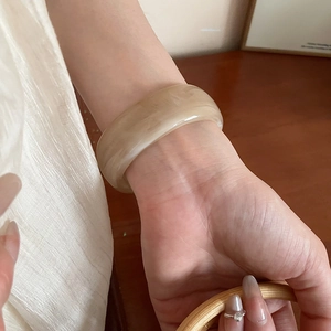 Close-up of beige marble pattern resin wide bangle bracelet on wrist in warm light