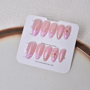 Detailed view of pink almond press-on nails with 3D floral accents and golden beads