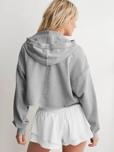 Detailansicht der Rückseite eines grauen Cropped-Hoodies mit Kapuze und überschnittenen Ärmeln