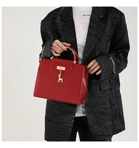 Detail of red crocodile texture handbag with golden deer charm and metal handle