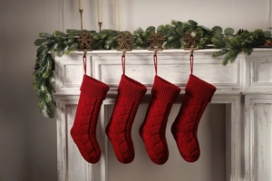 Close-up of four red knitted Christmas stockings with classic cable patterns on a fireplace