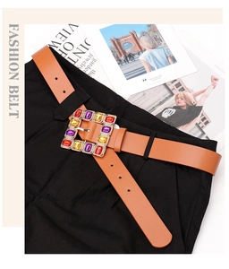Detail of a brown leather belt with a square gold buckle featuring colorful gemstones