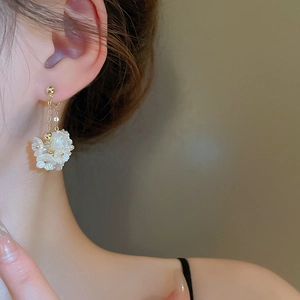 Detailaufnahme von goldenen Quastenohrringen mit weißen Blumen am Model getragen