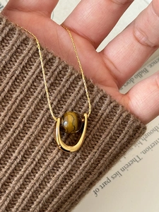 Macro detail of U-shaped gold necklace with tiger eye stone on brown knit sweater