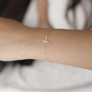 Detailed view of a slender gold cross bracelet with micro-pave crystals on the wrist
