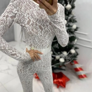 Detail of white floral lace jumpsuit with long sleeves in front of a Christmas tree decor