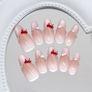 Pink cat eye press-on nails with red 3D bows and rhinestones on a mirror tray