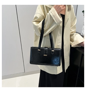 Detail of a minimalist black glossy leather shoulder bag with elegant gold hardware buckles