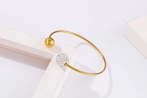 Détail d'un bracelet ouvert doré en C avec une bille polie et une sphère sertie de strass