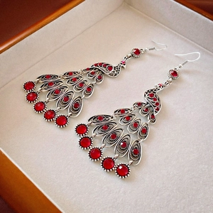 Detailed view of vintage peacock tassel earrings with red crystals in a jewelry box