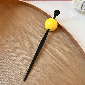 Detail of modern hair stick with yellow sphere on wooden tray against clean background