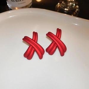Detail shot of red matte X-shaped cross knot stud earrings on white ceramic tray