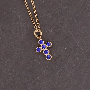 Macro shot of gold cross pendant with six inlaid blue gemstones on a stone surface