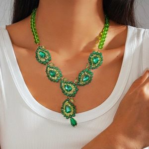 Dettaglio di ciondoli a goccia verde smeraldo su una collana boho con perline dorate