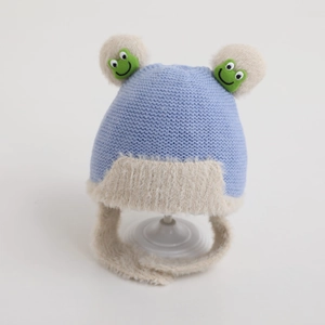 Detailed knit of infant earflap hat with blue yarn and cute green frog embroidery