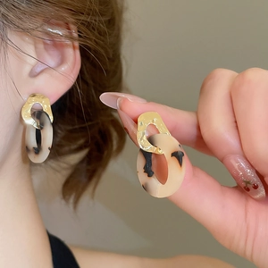 Close-up of leopard acetate and hammered metal hoop earrings worn by a model