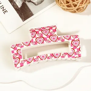Macro view of a large pink checkered hair claw clip with heart patterns and glossy finish