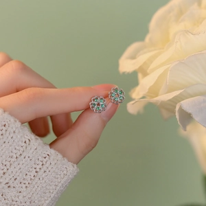 S925 sterling silver flower stud earrings featuring green zircon held by fingertips