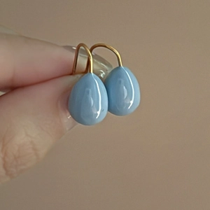 Detailed view of light blue teardrop earrings with gold hooks worn on ear