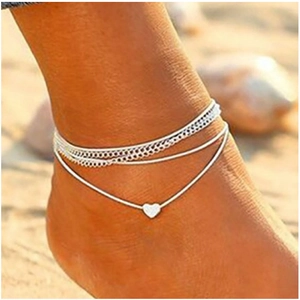 Detail of layered silver heart pendant anklet on foot with a beach background