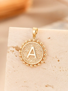 Macro shot of gold-plated pendant with embossed letter A and vintage beaded edge detail