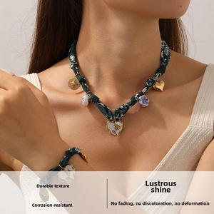 Detail of dark green woven necklace and bracelet set with golden heart and floral charms