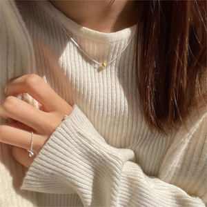 Close-up of minimalist gold bead pendant and silver necklace on a beige knit sweater