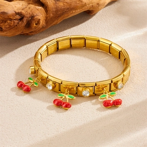 Gold stainless steel cherry charm bracelet with zircon inlay on sand background