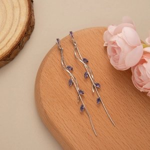 Detail view of long silver tassel earrings with purple marquise cut stones on wood base