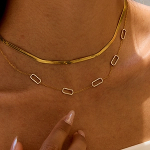 Close-up of layered golden snake chain and rectangular rhinestone pendant necklace