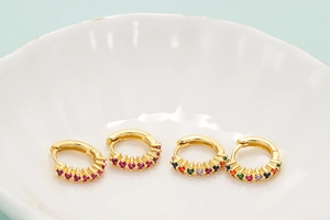 Macro shot of gold hoop earrings with colorful zircon inlay on a white shell plate