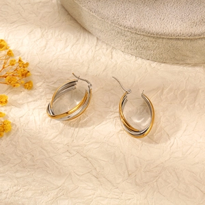 Détail de boucles d'oreilles ovales bicolores or et argent sur un support texturé chic