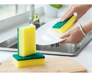 Close-up of dual-sided yellow and green cleaning sponge on a wooden board in the kitchen