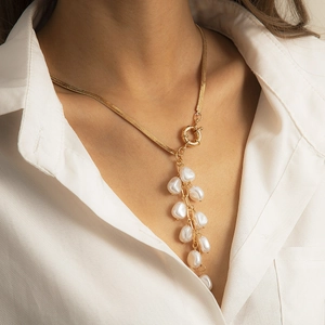 Detailed shot of a gold necklace featuring a round clasp and white baroque pearls on a model