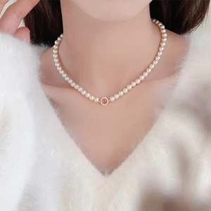 Primo piano di una collana di perle con ciondolo in pietra rosa su maglione bianco