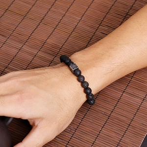 Close-up of men's volcanic stone beaded bracelet with vintage silver cross metal charm