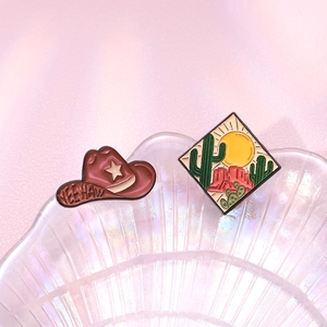 Western cowboy enamel pins with Yeehaw hat and desert landscape on pink shell plate