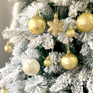 Dettaglio di ornamenti natalizi oro e bianchi appesi a un ramo d'albero innevato