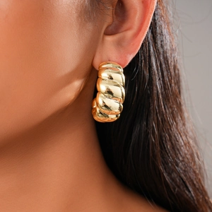 Close-up of a woman wearing gold twisted hoop earrings with a textured croissant style