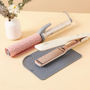 Hair straightener and curling iron on a grey heat-resistant silicone mat