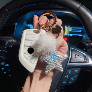 Sparkly star keychain with white mink fur ball and TPU key case held in car interior