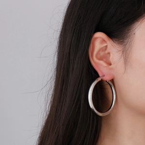 Close-up of minimalist large silver hoop earrings worn by a model to show actual size